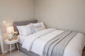 A neatly made bed with a grey headboard, a bedside table with a lamp, and a vase with flowers. - Experience Oslo from the front row (Oslo)