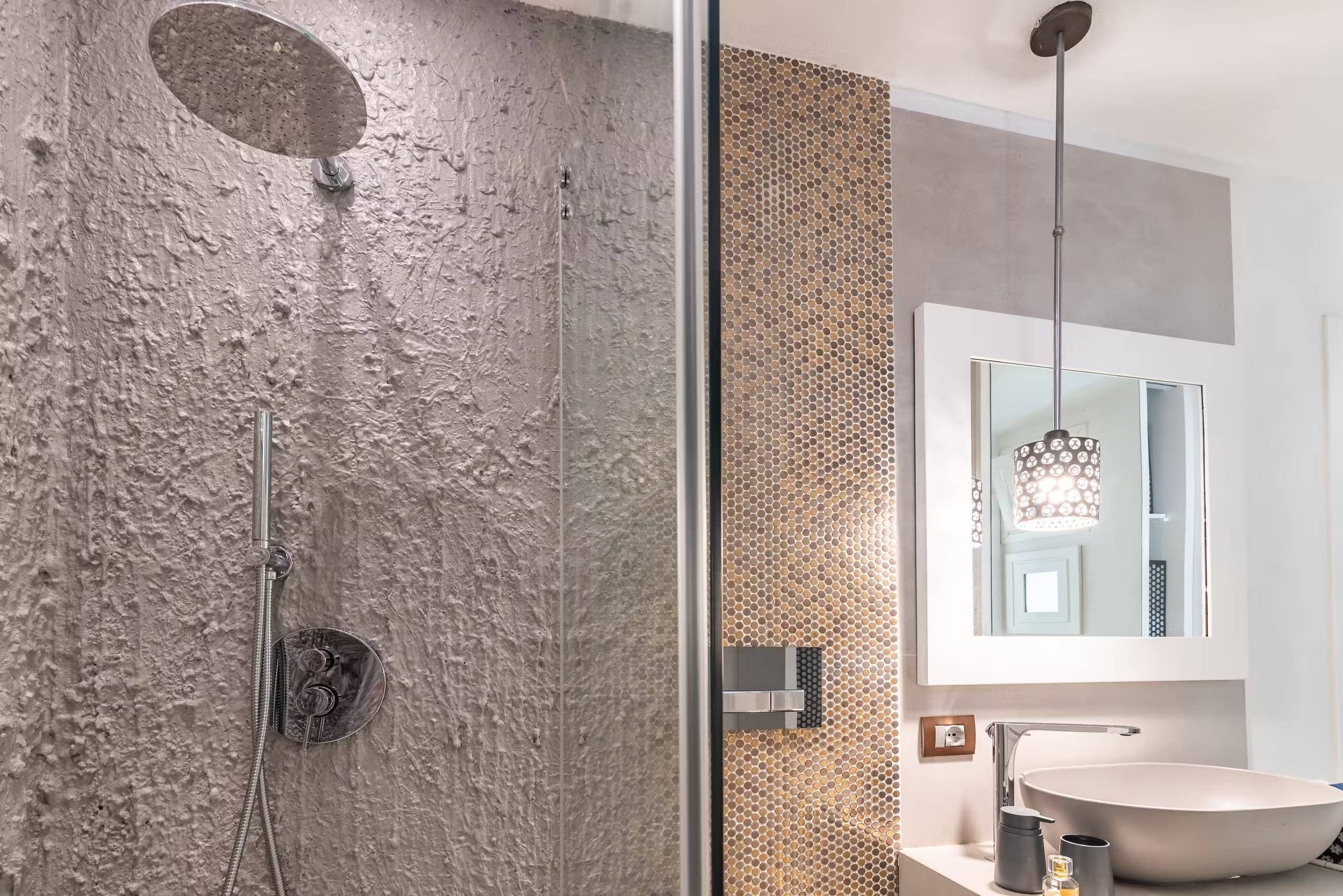 Ein modernes Badezimmer mit strukturierter Wand, einer Duschkabine aus Glas, einem großen Spiegel und einem runden Waschbecken.
