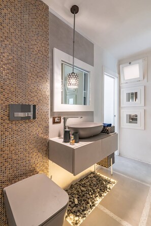 Un bagno moderno con un grande specchio, un lavandino rotondo e un water.