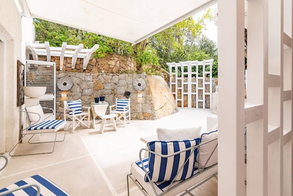 Un espace extérieur aménagé en terrasse, avec un mur en pierre, des meubles blancs et une pergola.