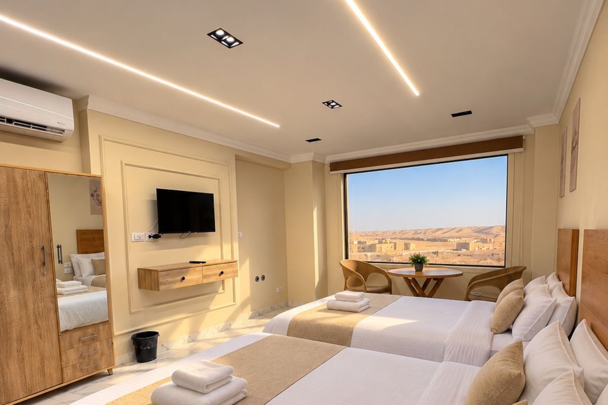 A hotel room with two beds, a TV, a window with a view, and a wooden wardrobe.