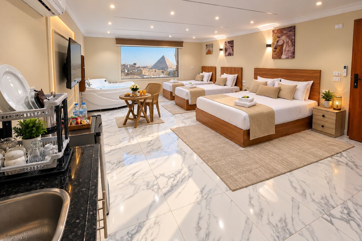 A hotel room with a large bed, two smaller beds, a dining area, a view of a pyramid, and a modern bathroom.