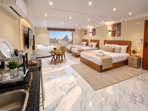 A hotel room with a large bed, two smaller beds, a dining area, a view of a pyramid, and a modern bathroom. - Wateen Pyramids View (Giza)