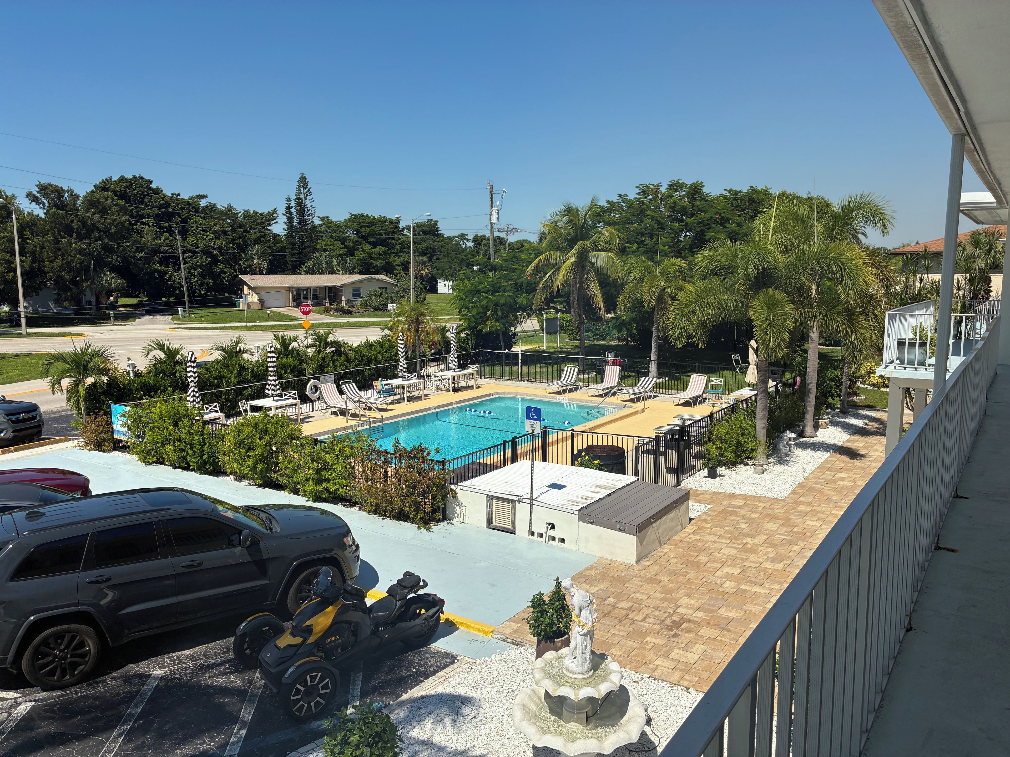 A swimming pool with lounge chairs, a statue, and a parking area with a motorcycle.