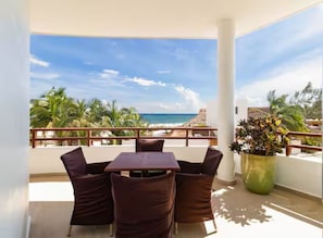 Ein Balkon mit Tisch und Stühlen, der Blick auf einen Strand und Palmen freigibt.