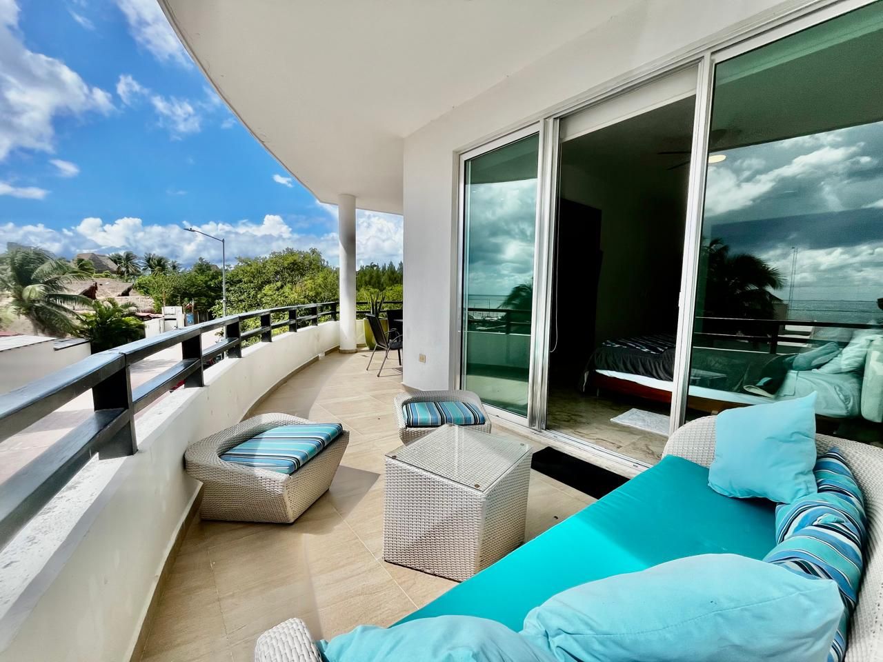 A balcony with wicker furniture, a teal sofa, and a glass door leading to a bedroom.