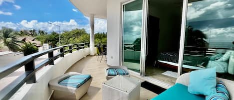 A balcony with wicker furniture, a teal sofa, and a glass door leading to a bedroom.