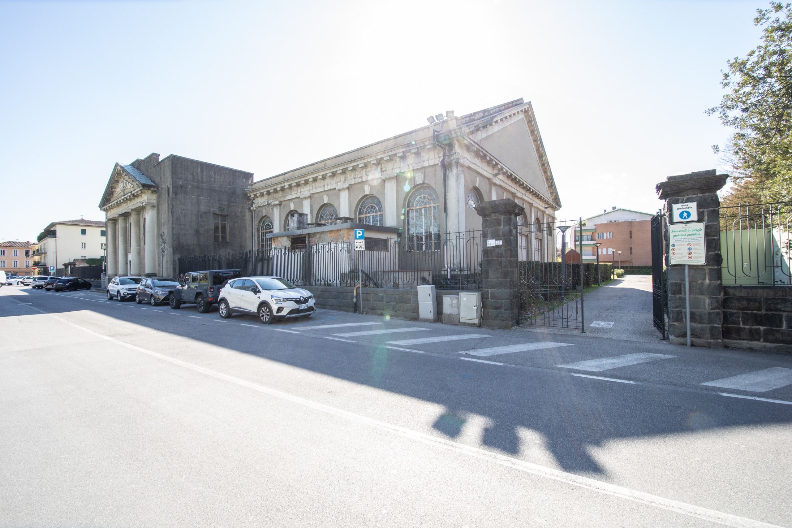 Een gebouw met klassieke architectuur, een hekpoort en geparkeerde auto's langs de straat.
