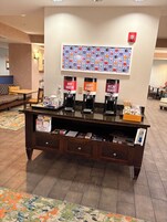 A hotel reception area with a coffee station, a wall with a colorful pattern, and a sofa in the background.