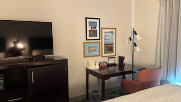 A hotel room with a bed, a desk with a lamp, a television, and framed pictures on the wall.