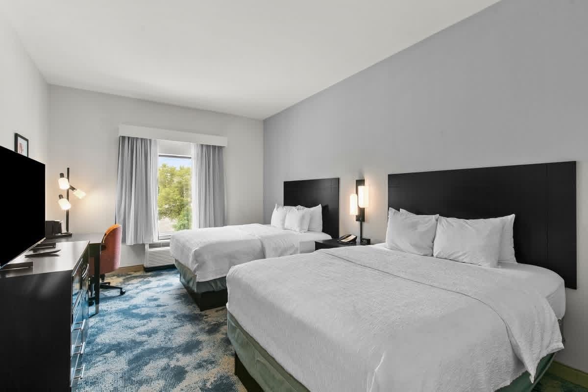 Ett hotellrum med två sängar, ett skrivbord, en stol och en tv.