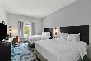A hotel room with two beds, a desk, a chair, and a TV.