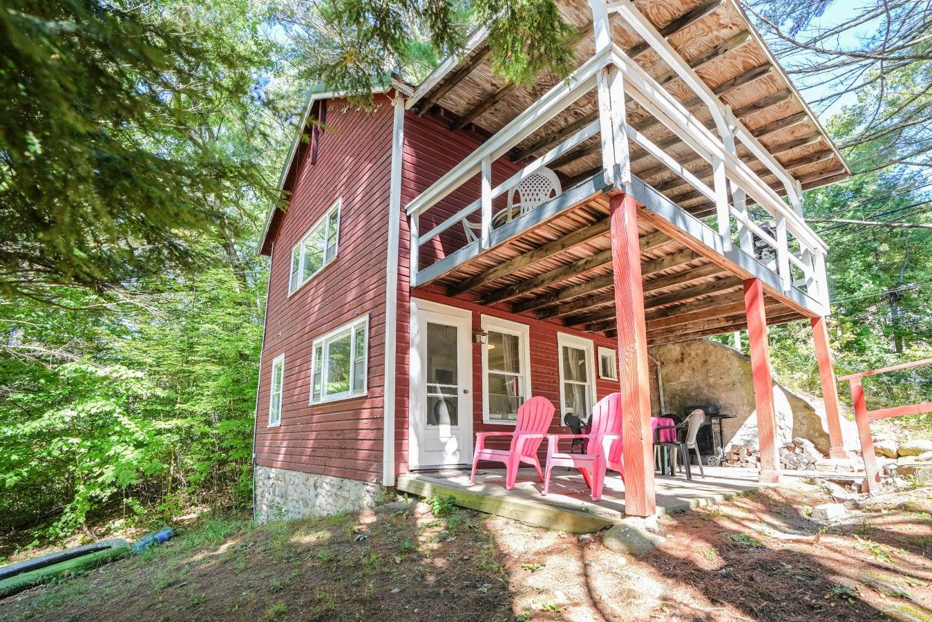 A red wooden cabin with a covered porch and pink chairs.