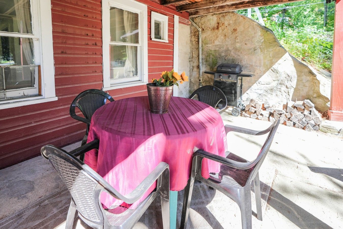Een terras buiten met een ronde tafel, afgedekt met een roze tafelkleed, omringd door vier stoelen.