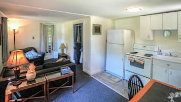 Ein gemütlicher, kleiner Wohnbereich mit Sofa, Tisch, Lampe, Kühlschrank, Herd und Spüle.