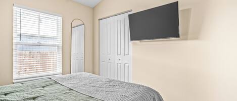 A bedroom with a bed, a TV mounted on the wall, and a window with blinds.