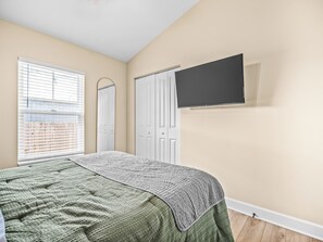 Une chambre à coucher avec un lit, un téléviseur fixé au mur et une fenêtre avec des stores.