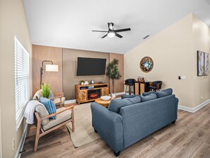 A living room with a sofa, chairs, a TV, a fireplace, and a ceiling fan.