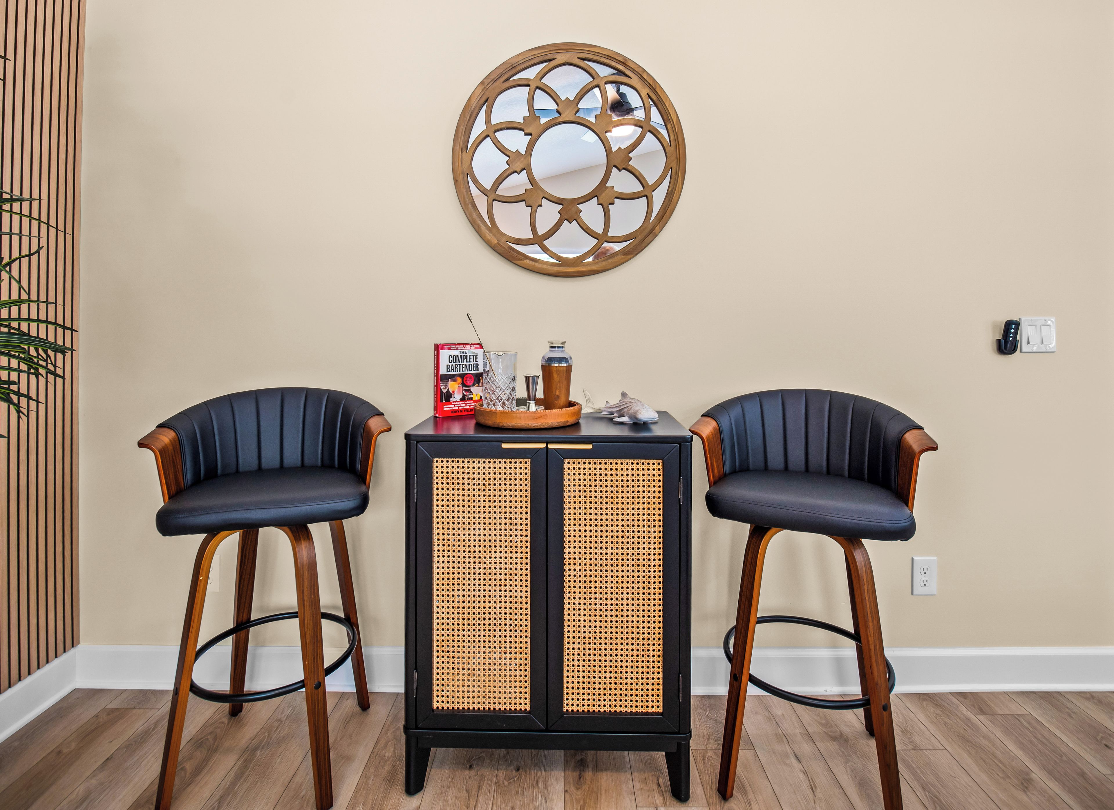 A room with two black upholstered chairs, a black and rattan side table, and a decorative wall piece.