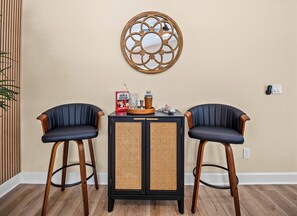 A room with two black upholstered chairs, a black and rattan side table, and a decorative wall piece.