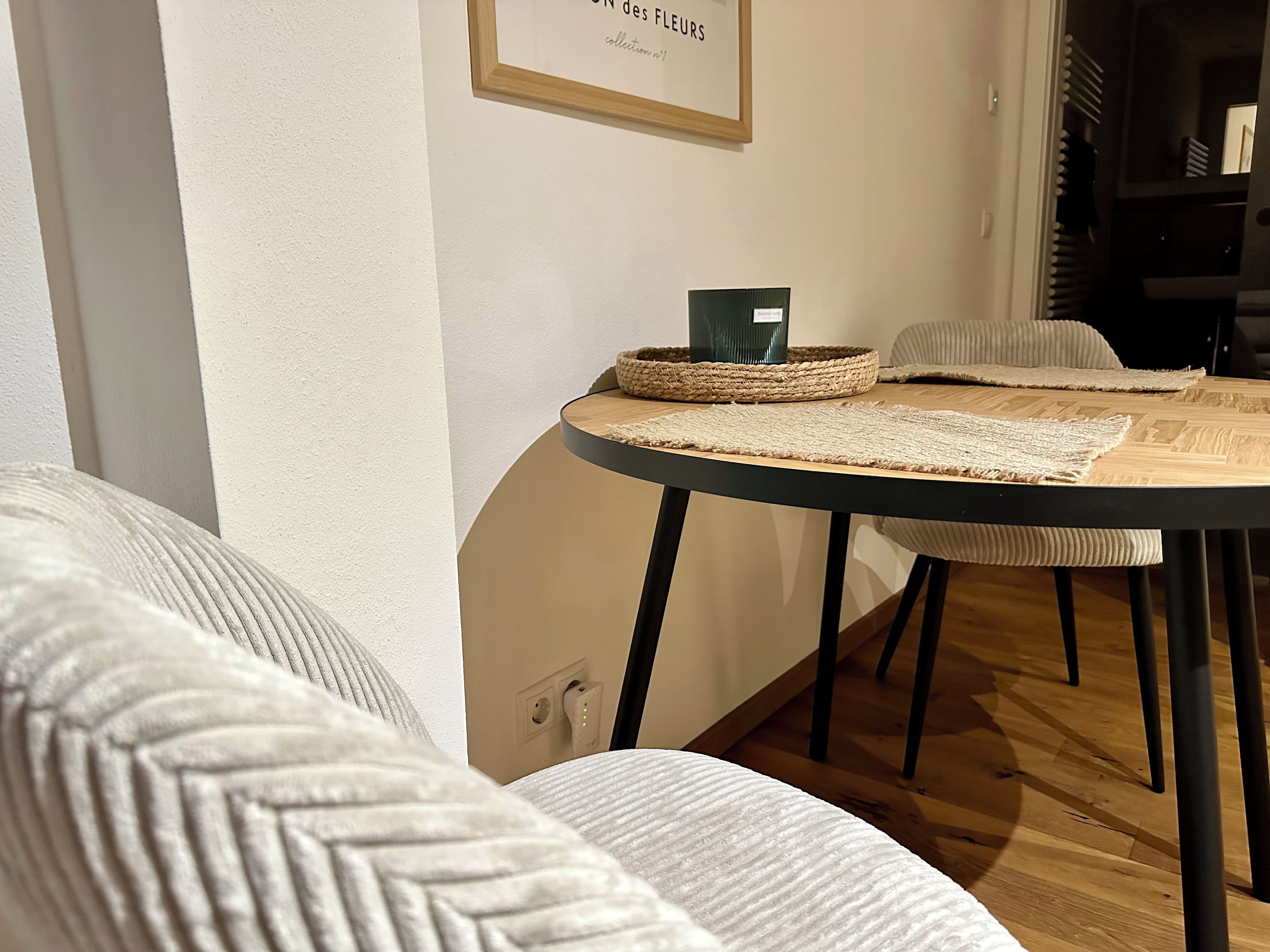 Um quarto com uma mesa redonda, duas cadeiras, uma cesta de vime e um texto emoldurado na parede.