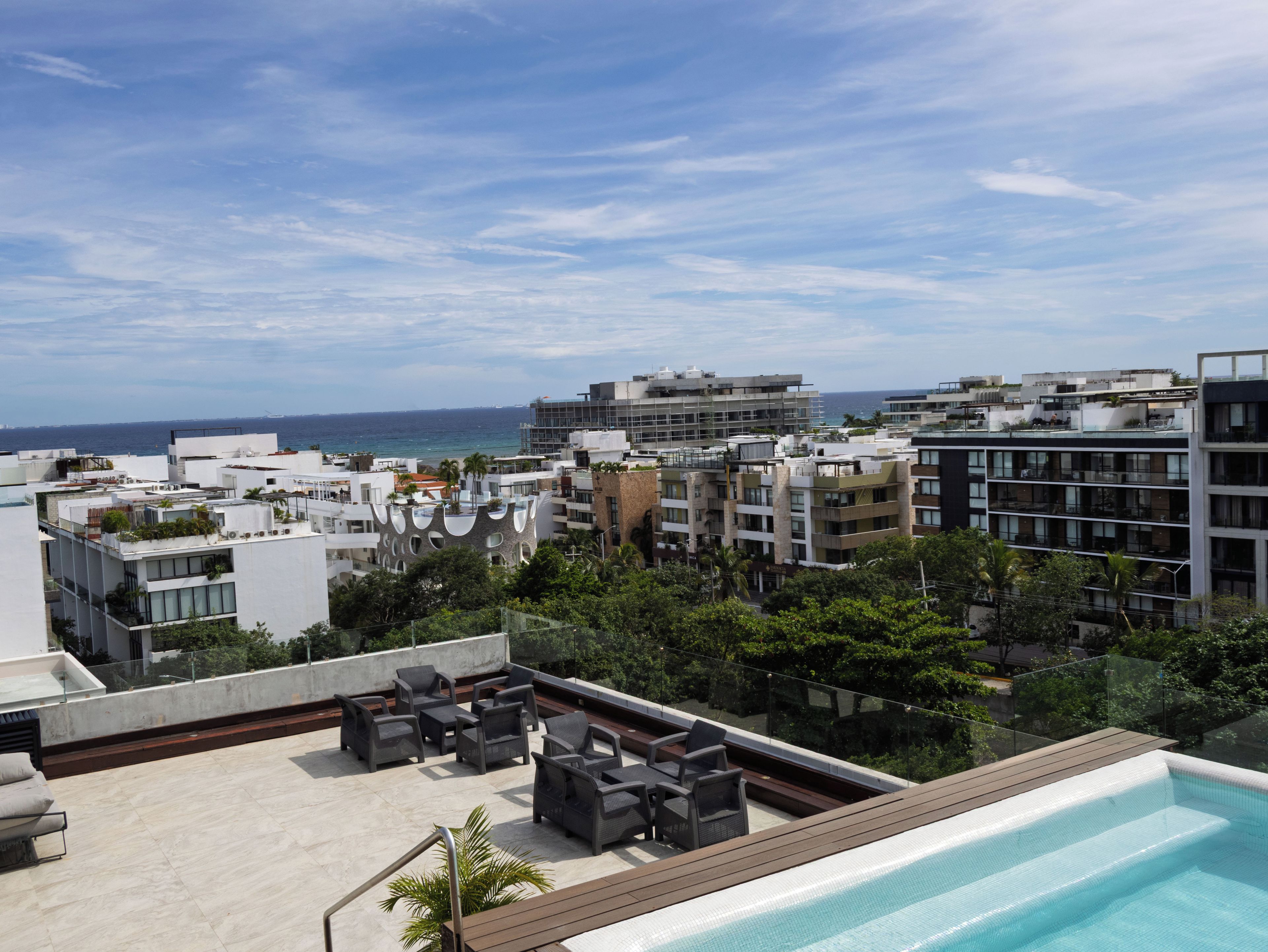 Une terrasse sur le toit avec une piscine, des espaces de détente en plein air et une vue sur le paysage urbain et l’océan.