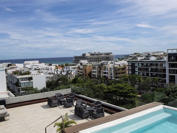 Una terraza en la azotea con piscina, mobiliario exterior y vistas a la ciudad y al océano.