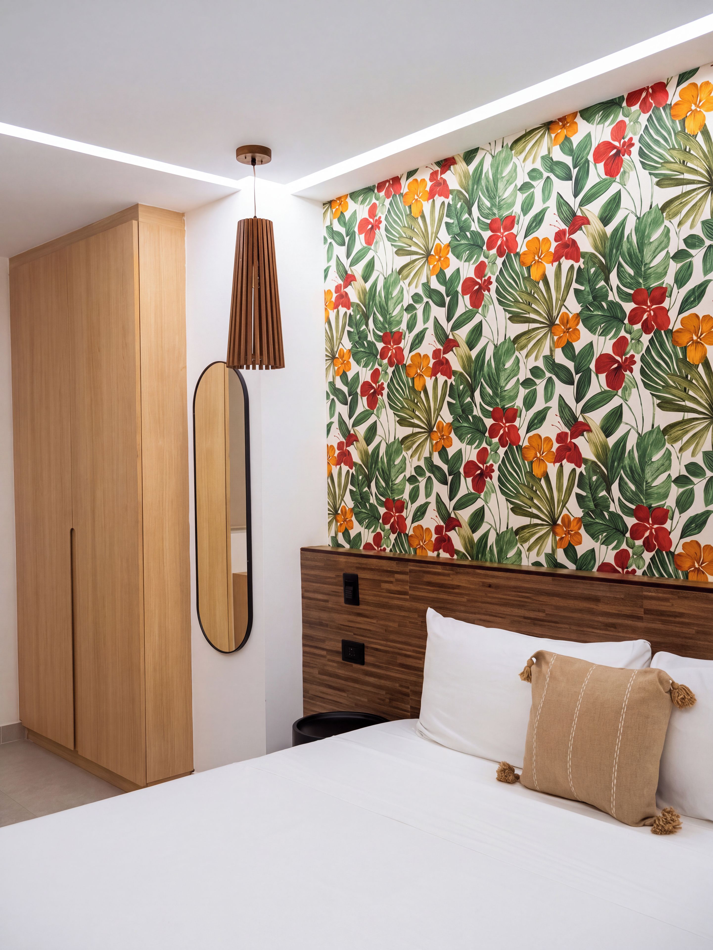 A bedroom with a bed, a wardrobe, a mirror, and a wall with a floral pattern.