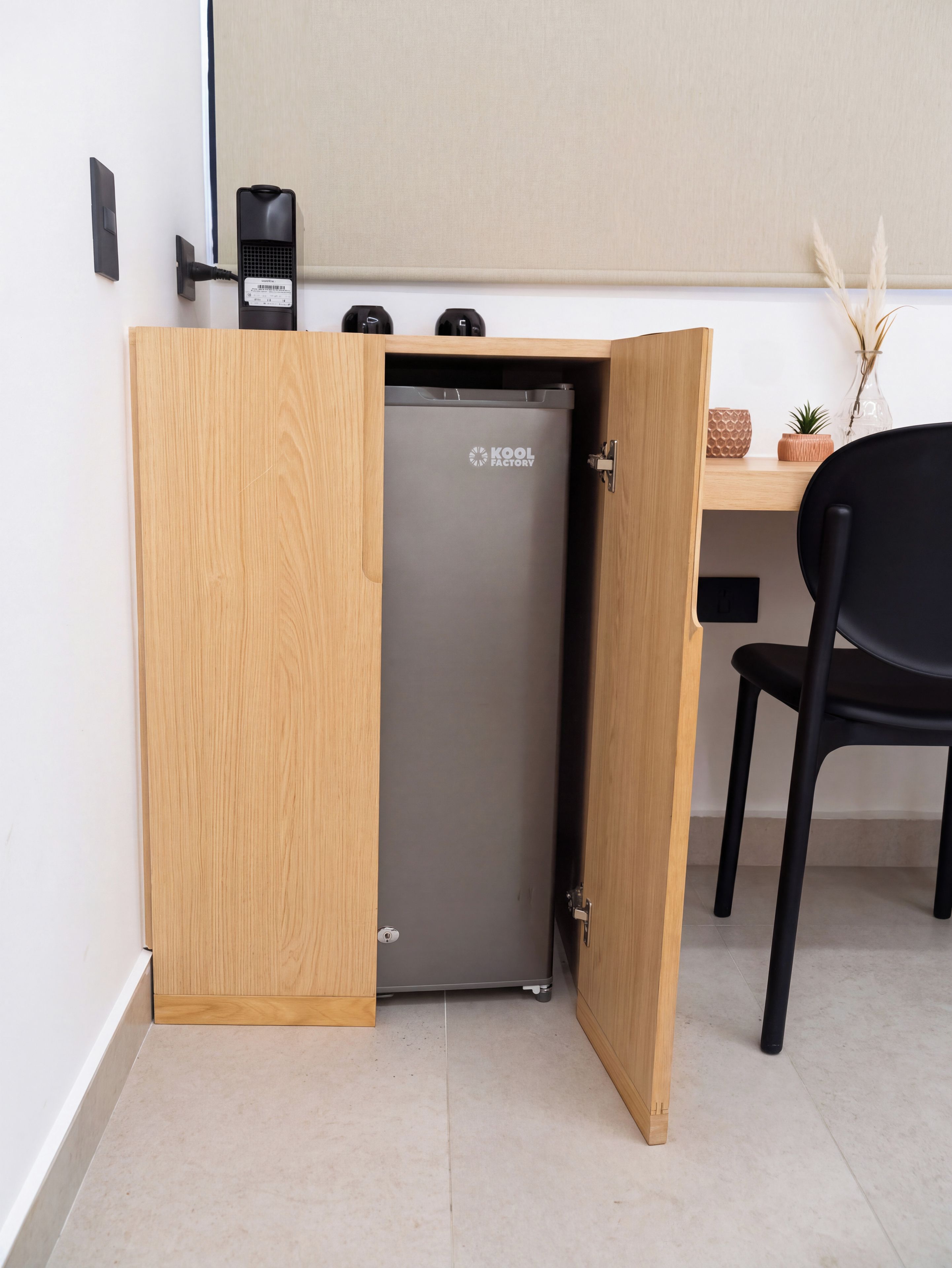 Eine kompakte Küchenzeile mit einem eingebauten Kühlschrank, einem Holzschrank und einem schwarzen Stuhl.