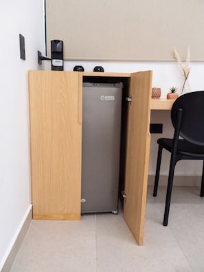 Una kitchenette compacta con refrigerador integrado, un armario de madera y una silla negra.
