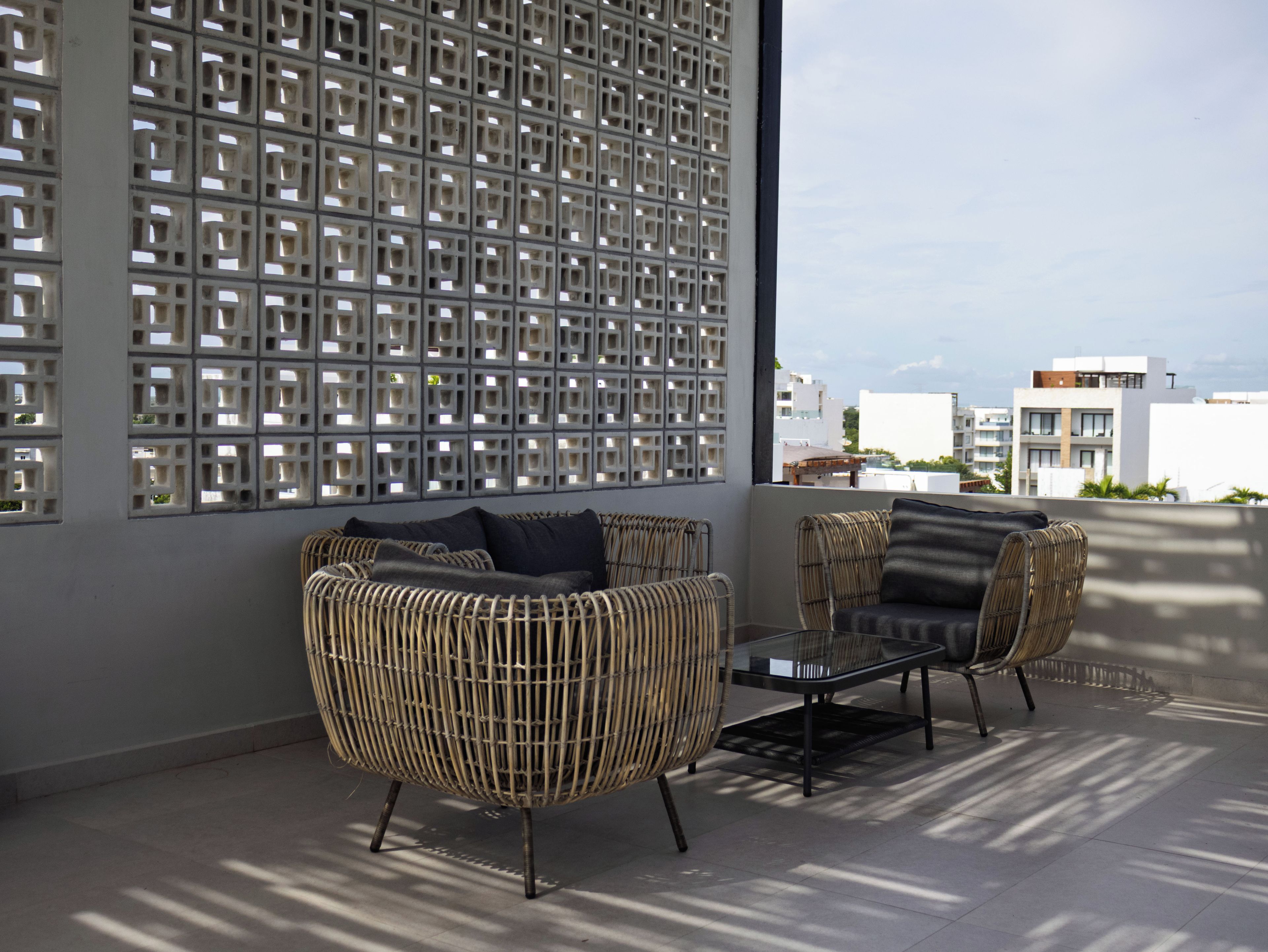 A balcony with wicker furniture and a glass table, overlooking a cityscape.