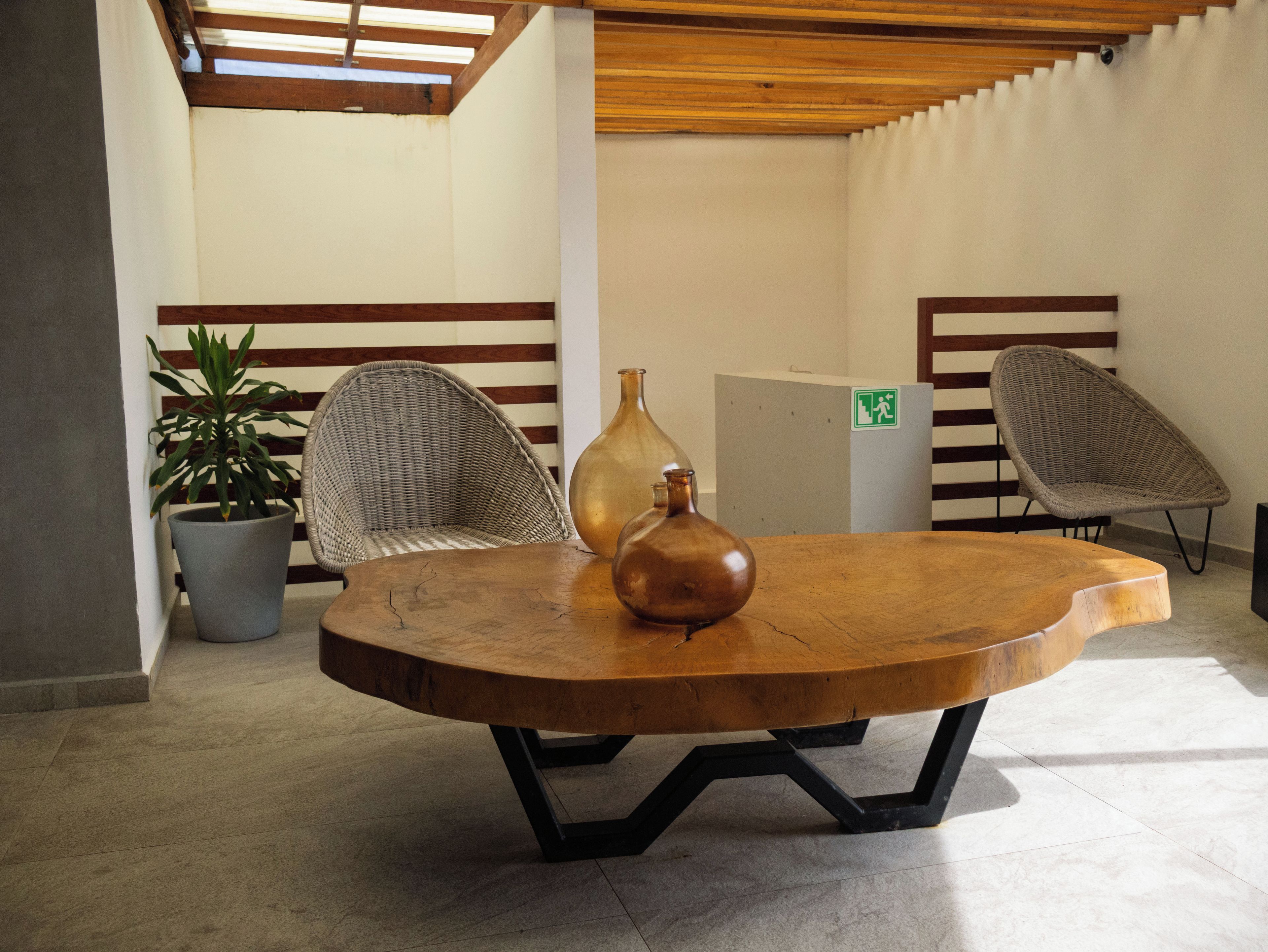 Une table ronde en bois avec des pieds en métal, deux chaises en osier, une plante en pot et un grand vase.