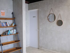 Una habitación con una puerta blanca, una estantería llena de libros y dos espejos colgados en la pared.