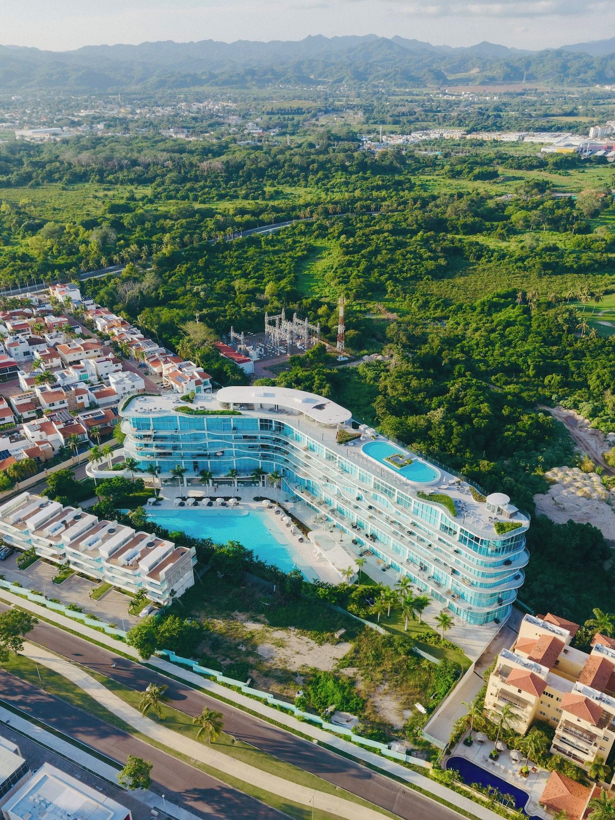 Un hôtel à plusieurs étages doté d’une piscine, entouré d’une végétation luxuriante et de bâtiments résidentiels.