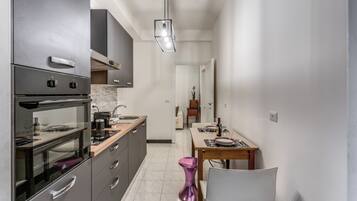 A modern kitchen with a built-in oven, a dining area with a table and chairs, and a hallway leading to a bedroom.