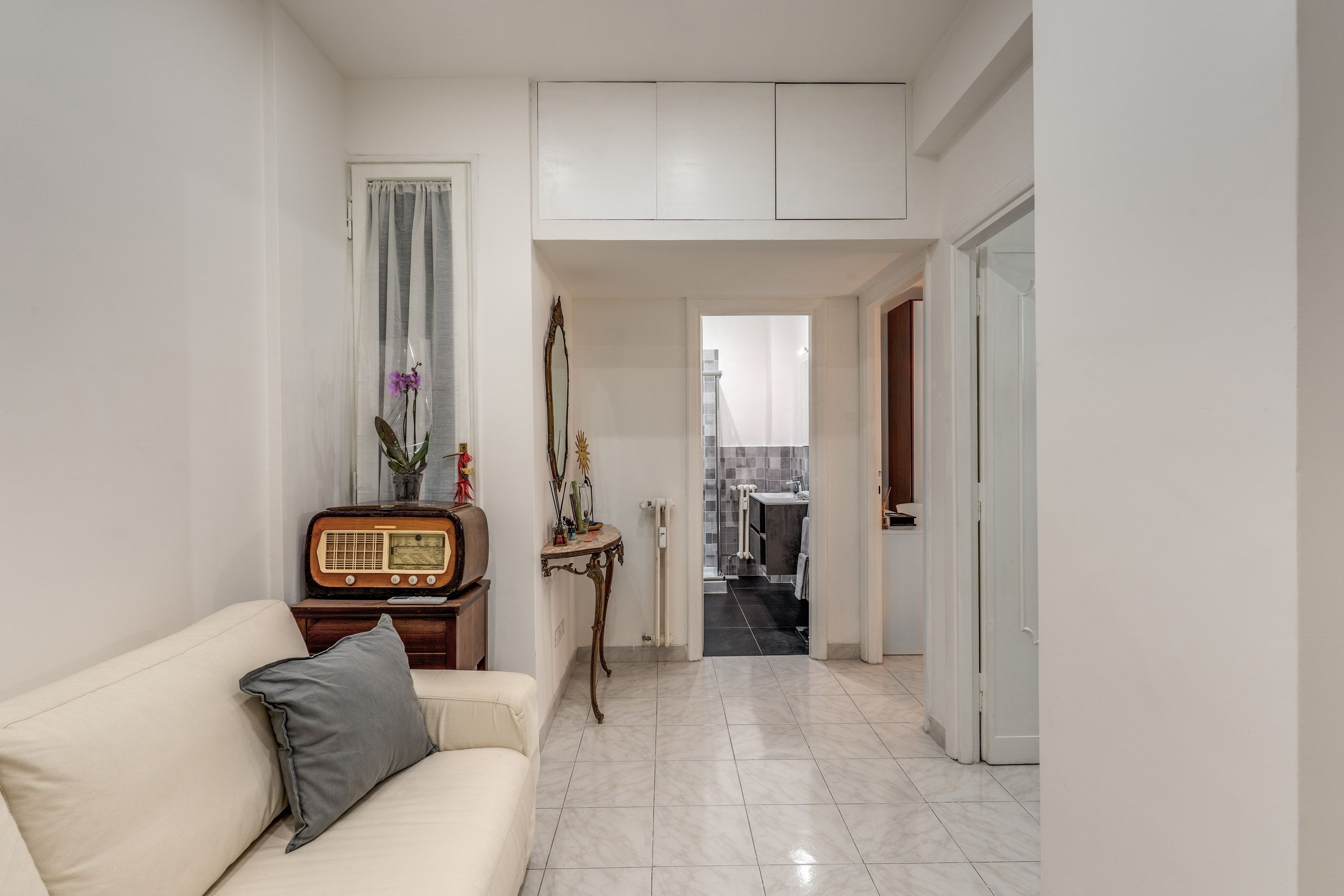 A hallway with a white sofa, a small table with a radio, and a mirror.