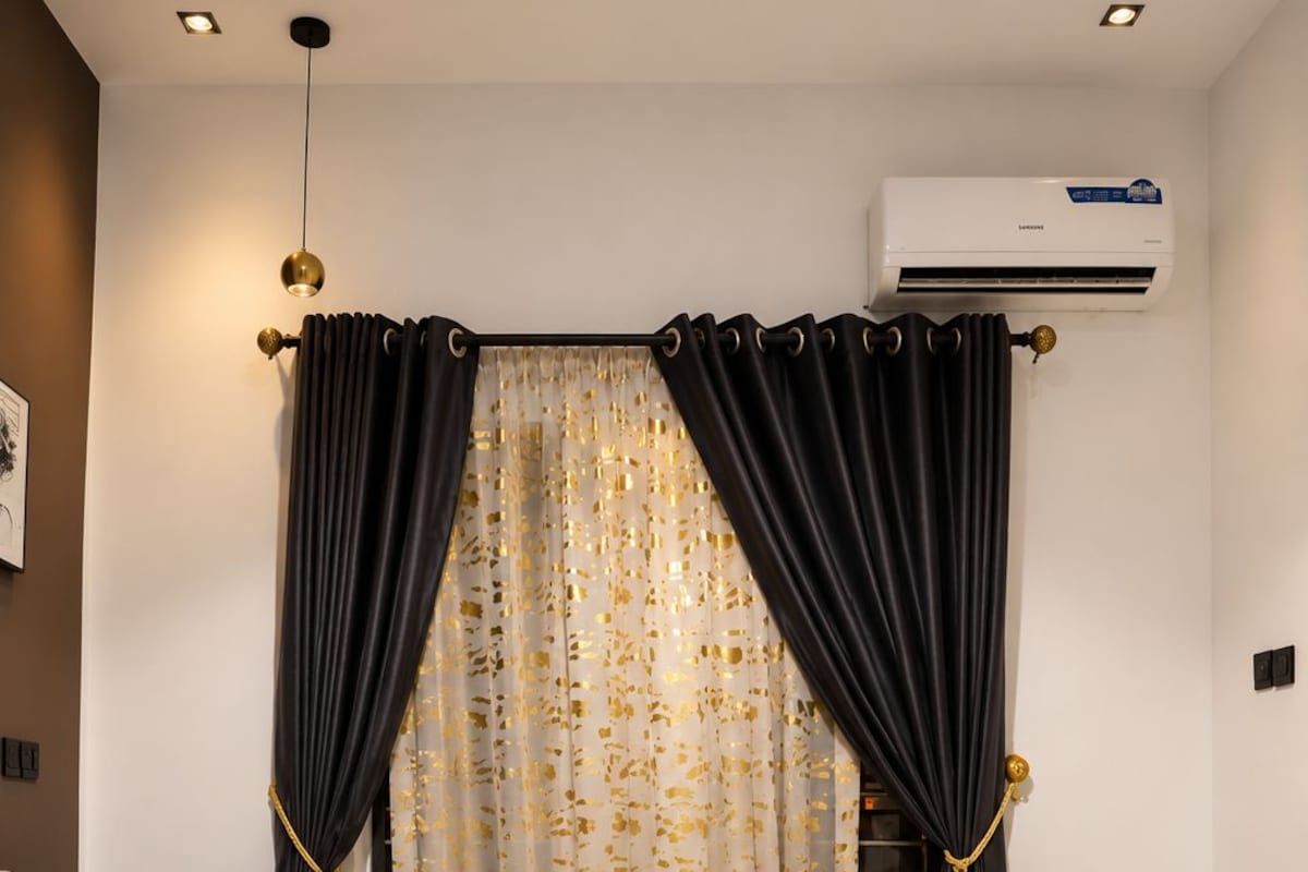 Quarto com cama, cortinas, aparelho de ar condicionado e luminária na parede.
