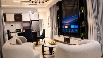 A modern living room with a flat-screen TV, seating area, and a kitchenette.
