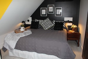 A bedroom with a large bed, a bedside table with a lamp, and a wall with framed pictures.