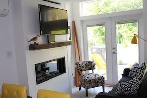 A living room with a flat-screen TV mounted on a wall, a fireplace below it, and a yellow chair in the foreground.