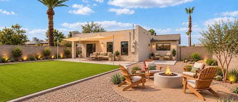 A modern outdoor patio with a fire pit, seating area, and a well-maintained lawn.