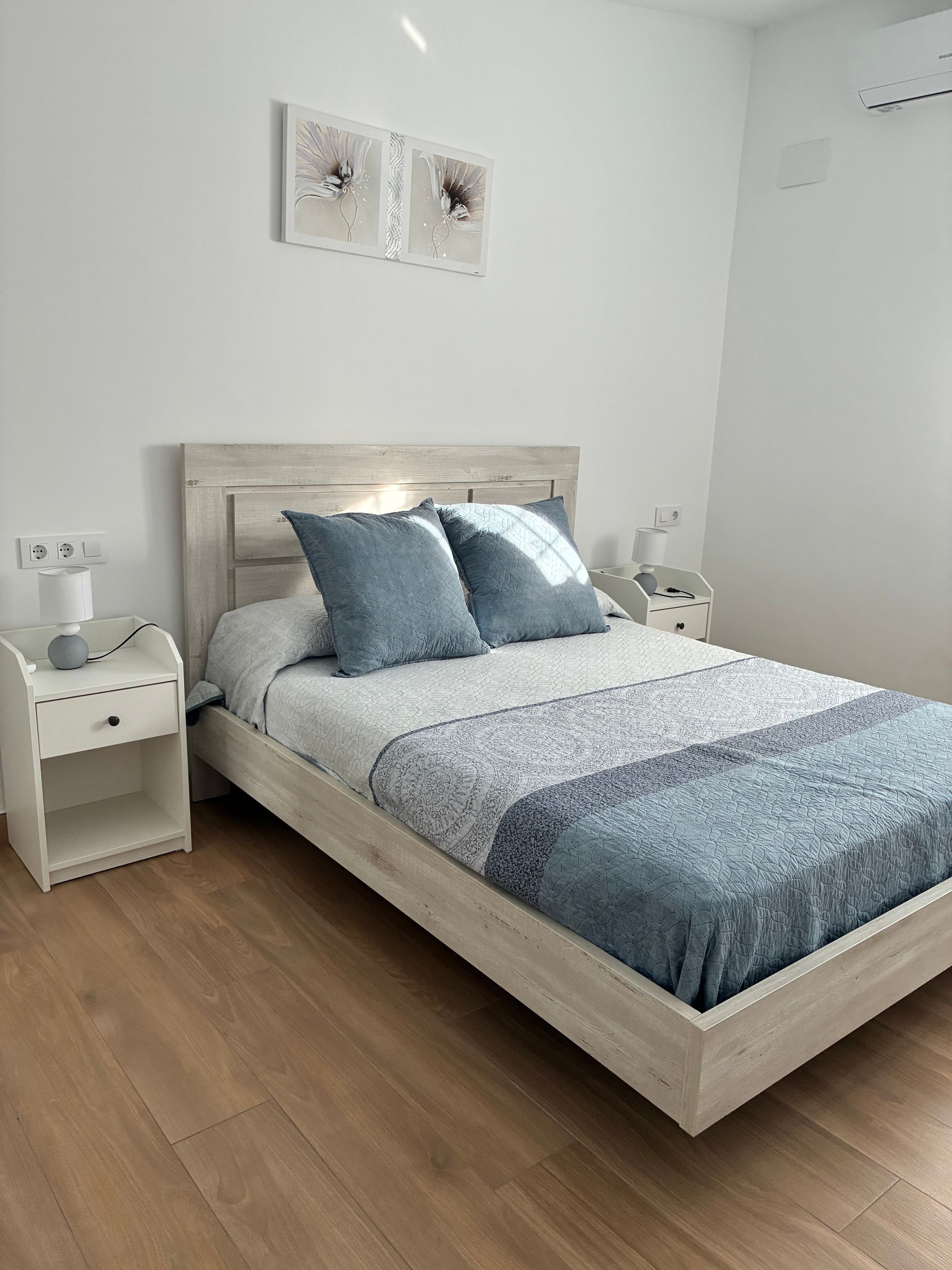 Ein Bett mit Holz-Kopfteil, zwei Nachttische und ein an der Wand hängendes Kunstwerk.