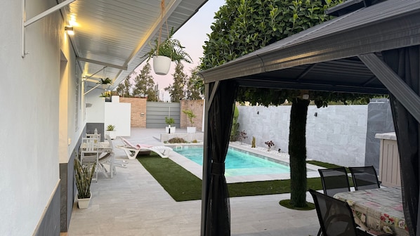 A covered outdoor area with a pool, seating, and a small garden.