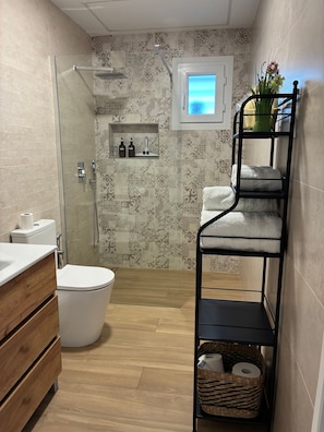 A compact bathroom with a shower, toilet, and a small window.