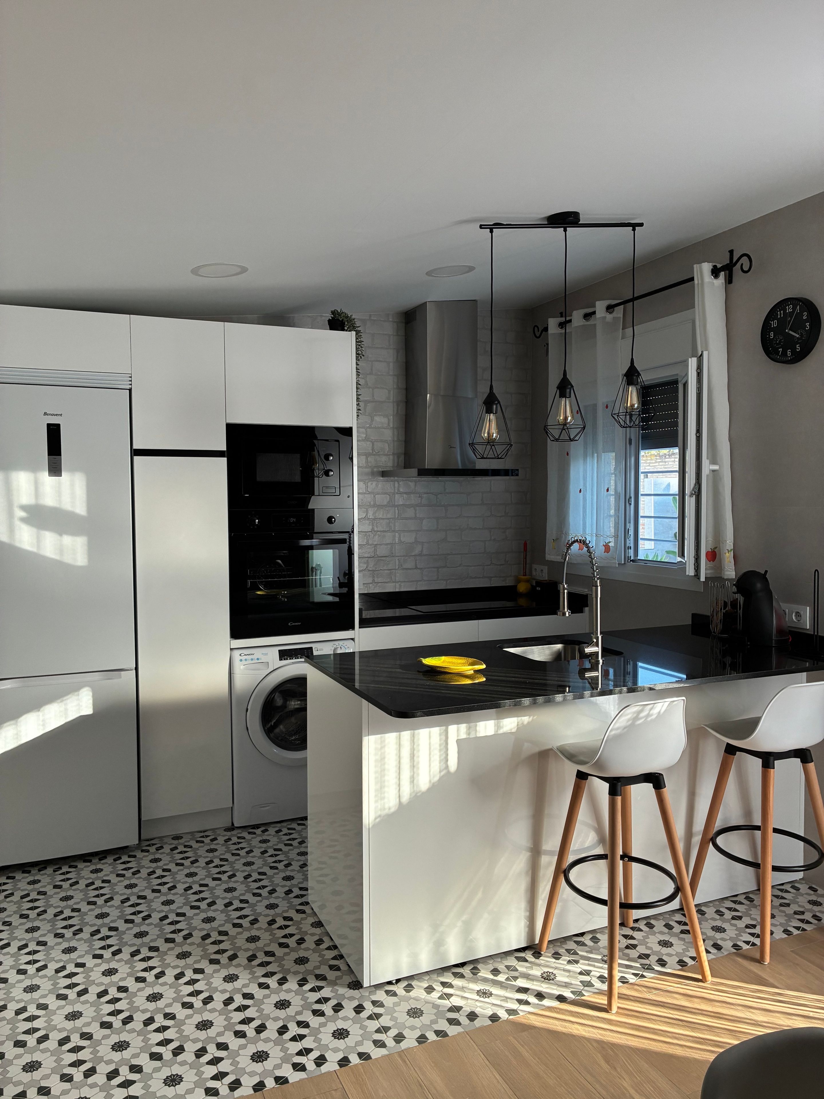 A modern kitchen with a central island, bar stools, a washing machine, and a built-in oven.