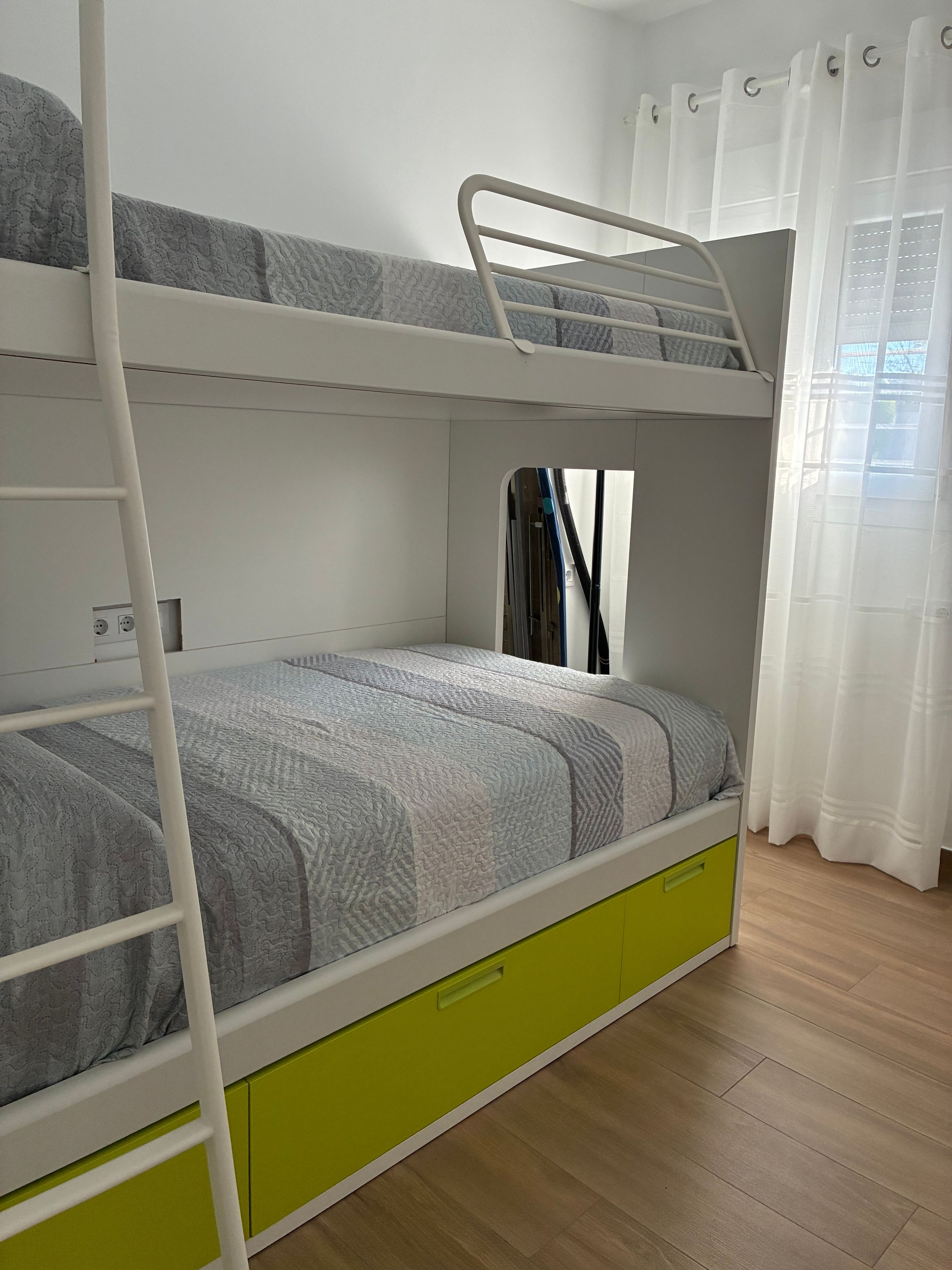 Uma cama de beliche com escada, uma cama de solteiro embaixo e uma gaveta verde.