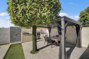 Eine Terrasse mit einer Pergola, Sitzgelegenheiten im Freien und einem Grillbereich.