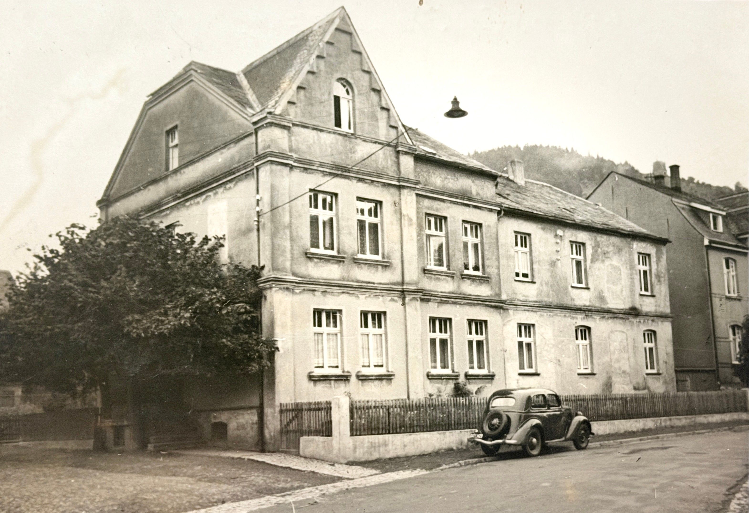 Ein großes, mehrstöckiges Gebäude mit einem markanten Giebeldach und einem Oldtimer davor.
