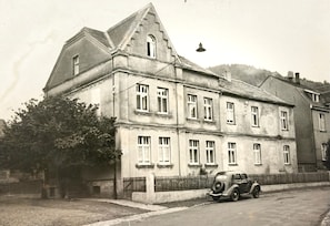 Ein großes, mehrstöckiges Gebäude mit einem markanten Giebeldach und einem Oldtimer davor.