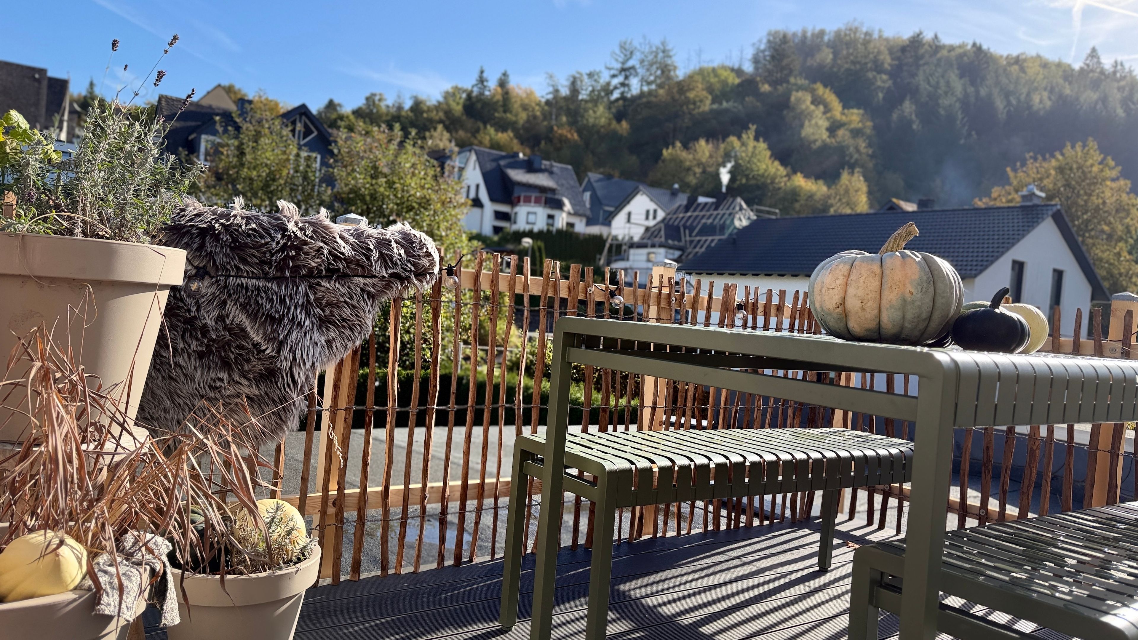 Eine Holzterrasse mit einem Metallstuhl und Tisch, einem Blumentopf und einem Kürbis auf dem Tisch.